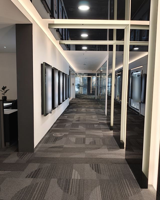 Corridor with lit ceiling frames, glass meeting rooms and framed pictures
